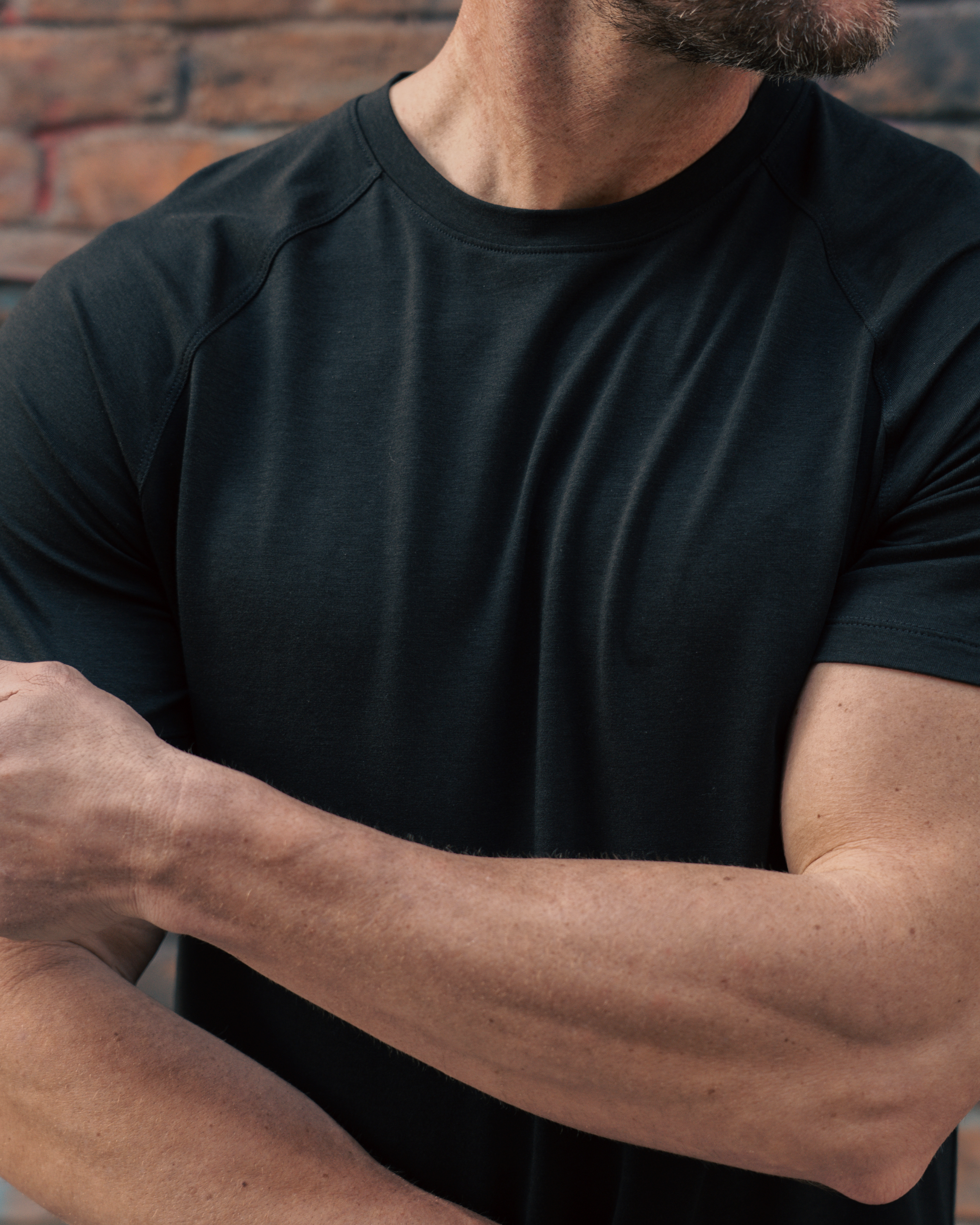 Person wearing a black t-shirt with a brick wall background