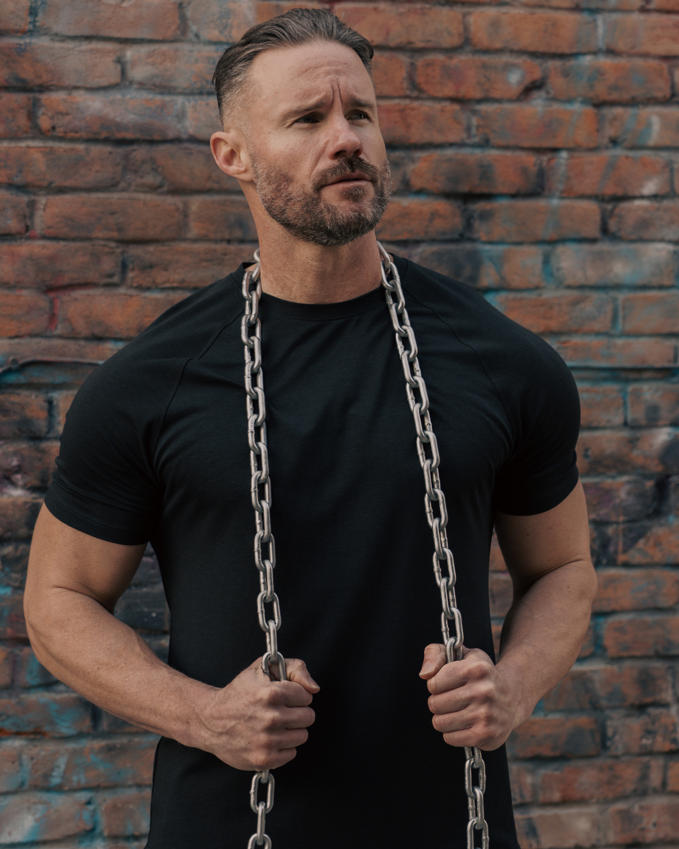 Man holding a chain against a brick wall