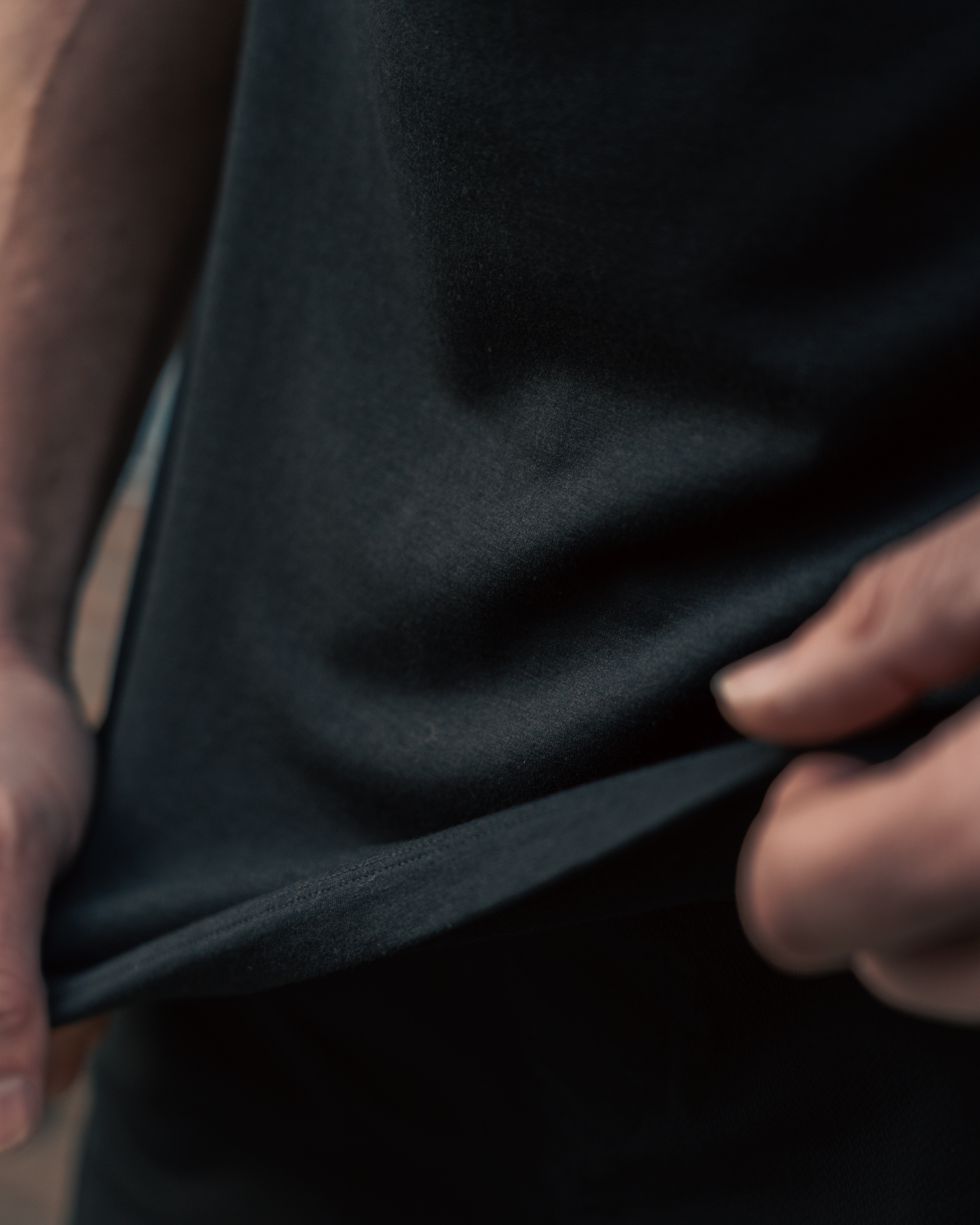 male wearing black drop cut crew shirt stretching black fabric