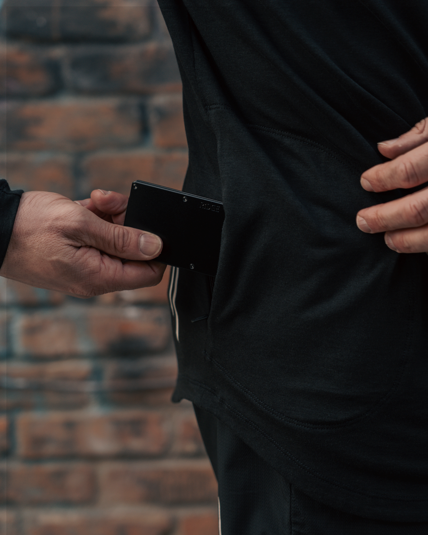 male wearing black hoodie placing wallet in side zip pocket of hoodie