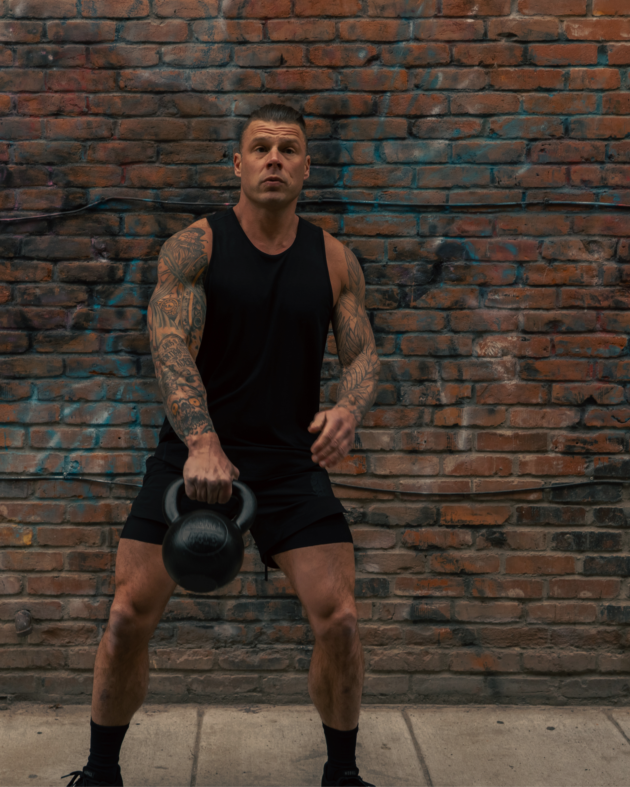 Man lifting a kettlebell against a brick wall