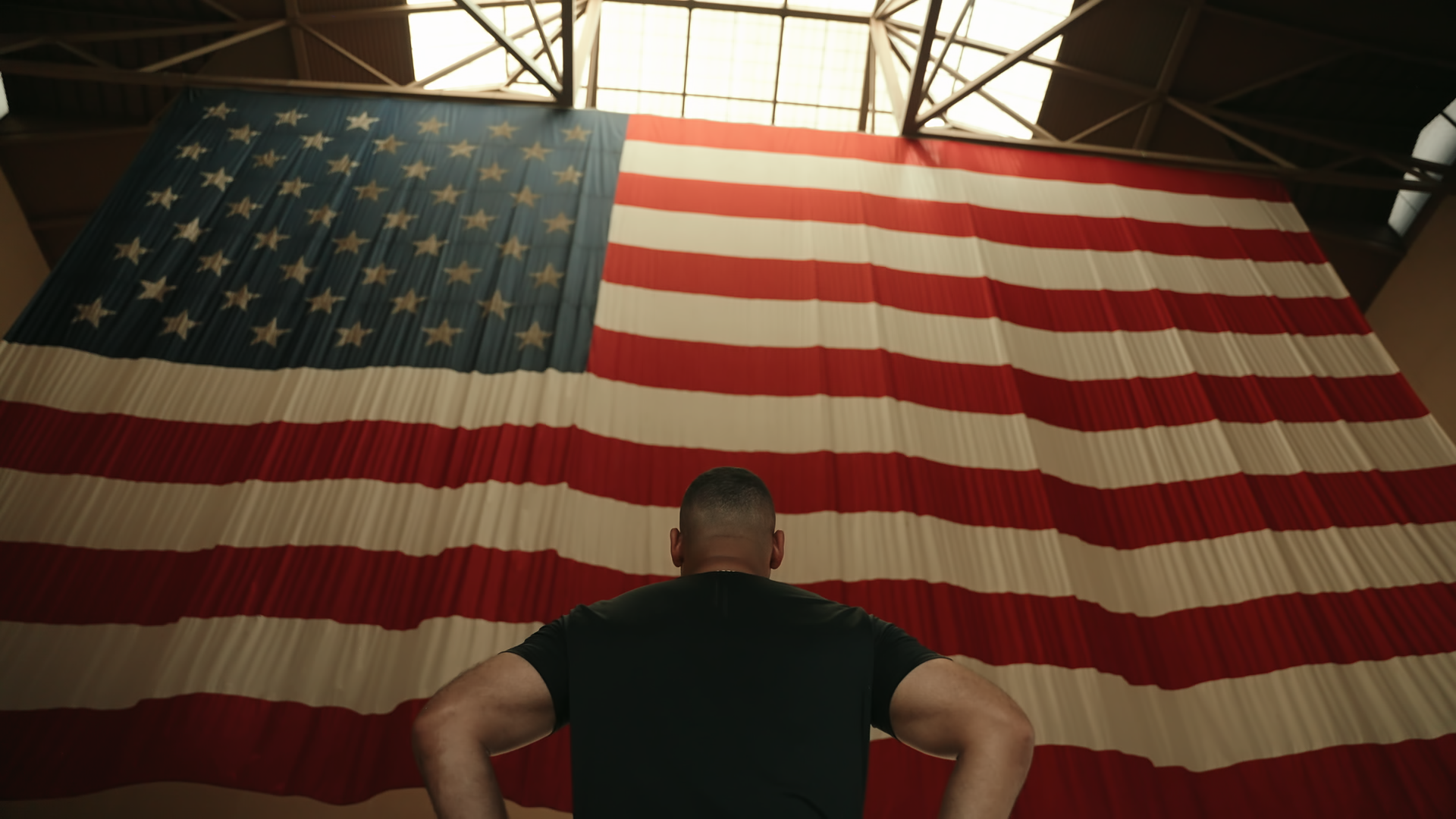 Jeremy Hudson standing in front of a large American flag indoors wearing the LINEAR baseline series night ops black shirt