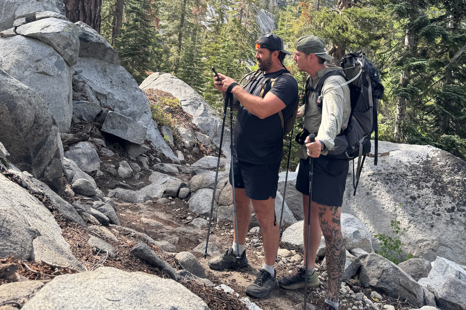 Navy SEAL Kyle Reed with another hiker on a rocky trail in a mountainous area with trees and rocks around.
