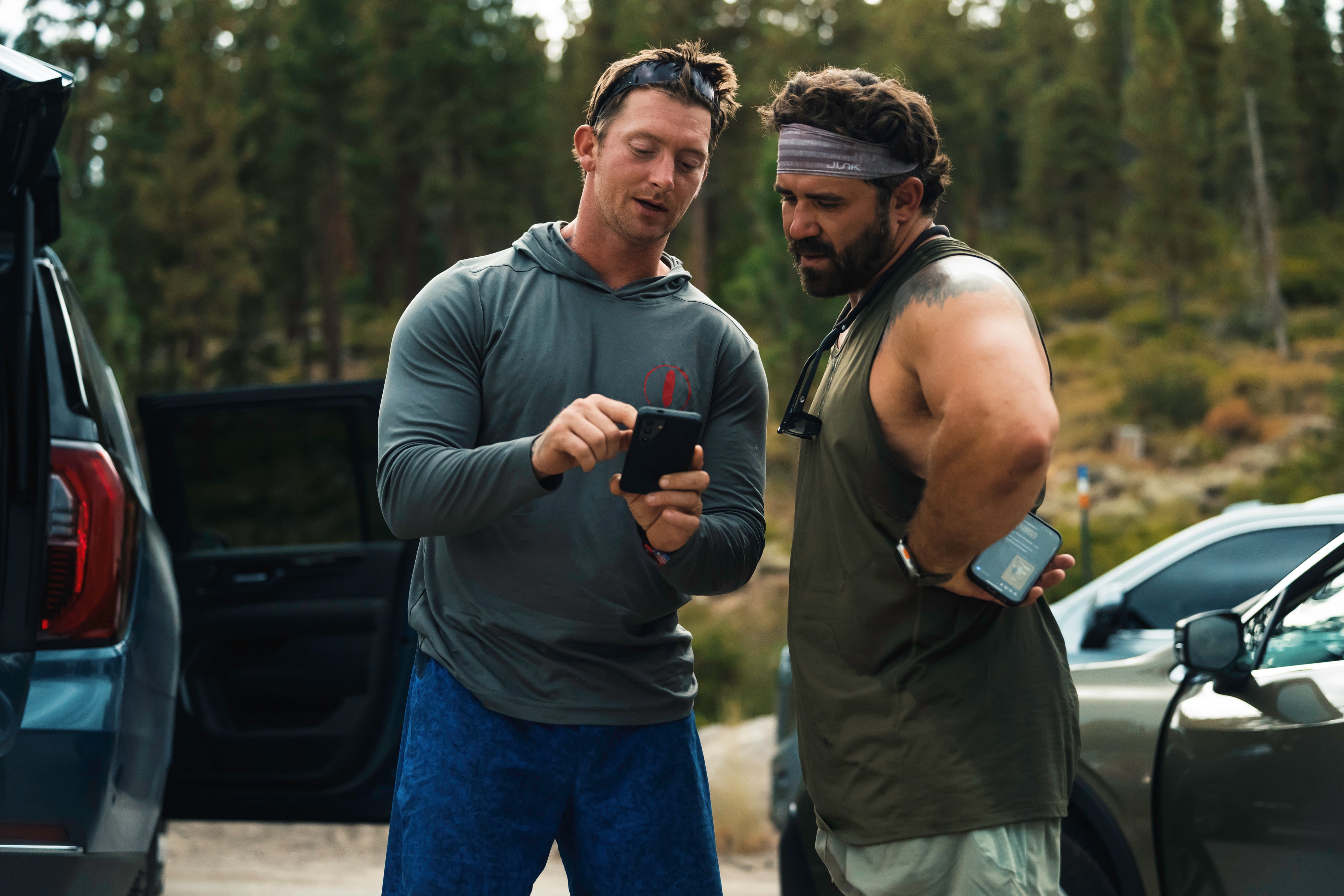 Navy Seal Kyle Reed standing outdoors with another man who is using a phone, with cars and trees in the background during the 20 Mountain 220