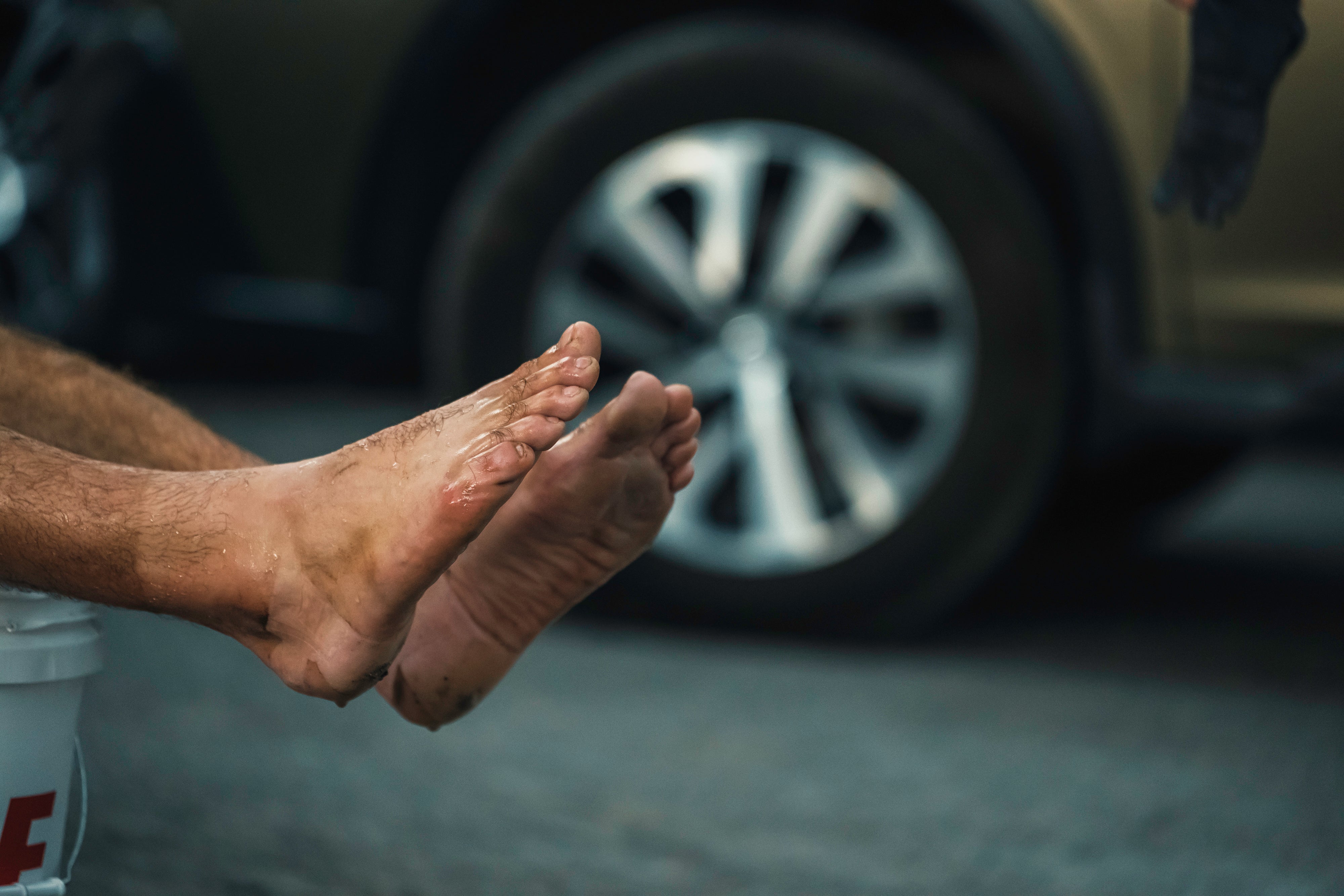 Close-up of Navy Seal Kyle Reed's swollen feet after soaking them in ice water with a blurred car tire in the background.