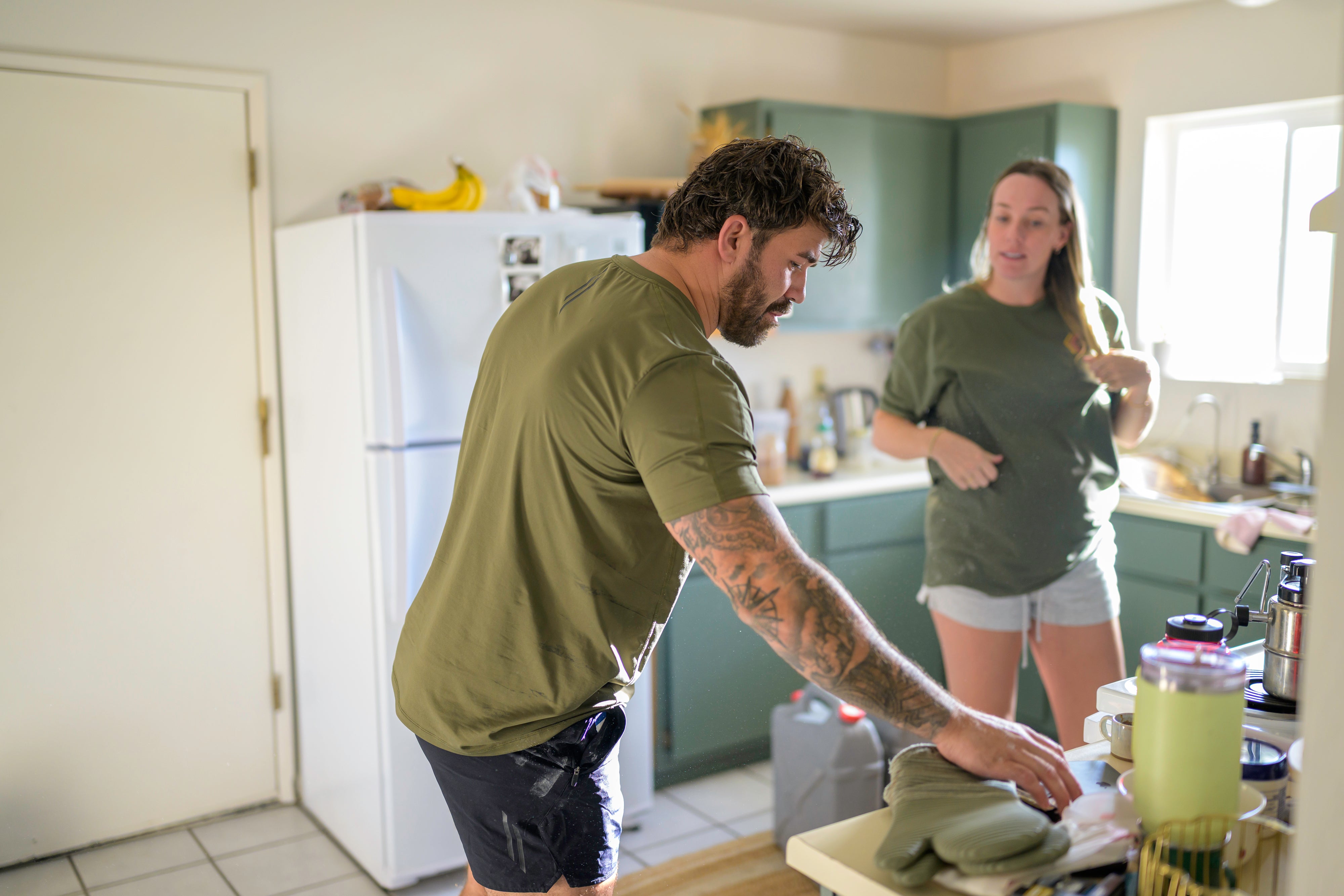Navy Seal Kyle Reed wearing LINEAR baseline ODA Green shirt and Night Ops Black baseline shorts in a kitchen preparing food on a stove with woman in the background during the 20 Mountain 220.