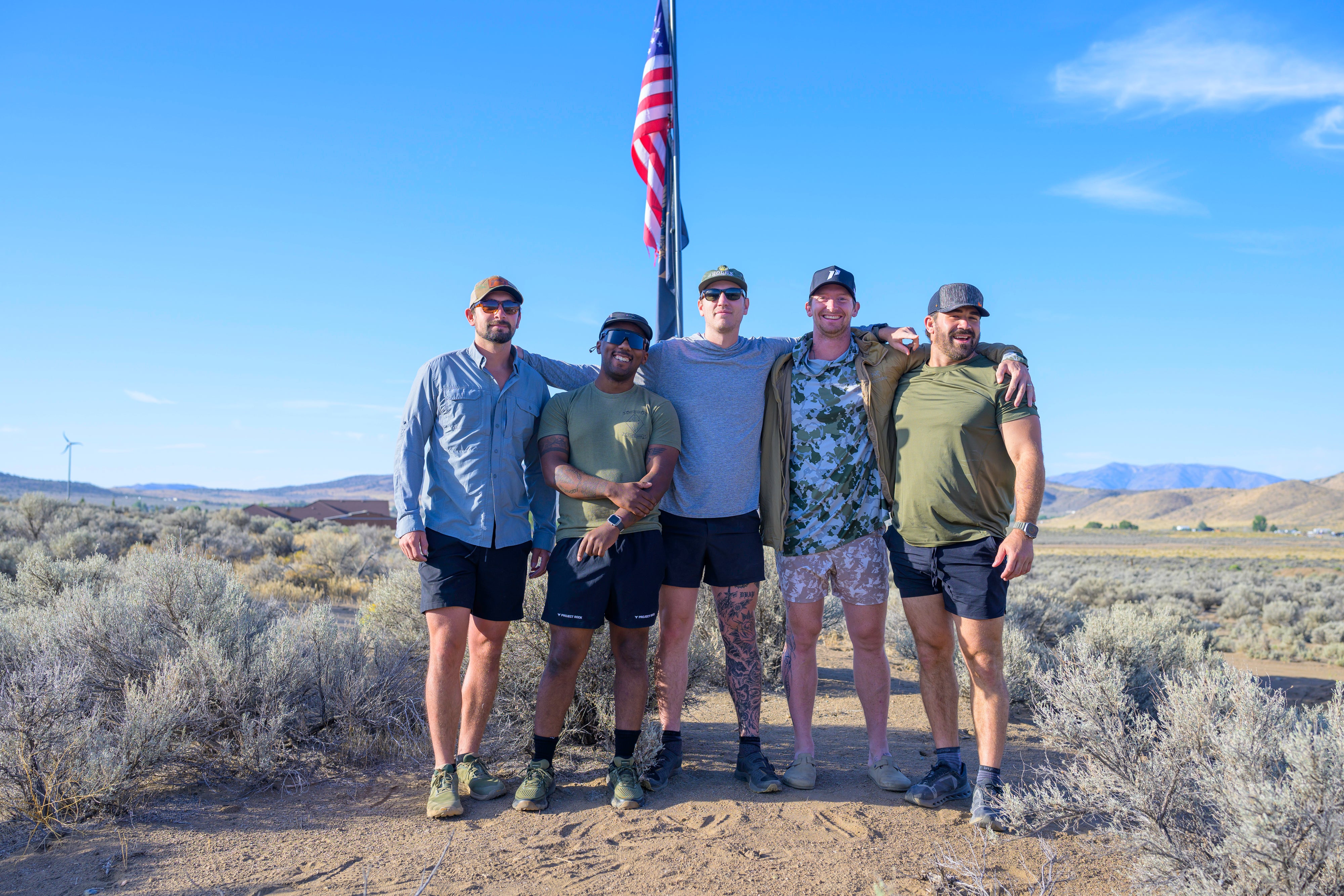 Navy Seal Kyle Reed standing with four other men together in a desert landscape with an American flag in the background during the 20 Mountain 220.