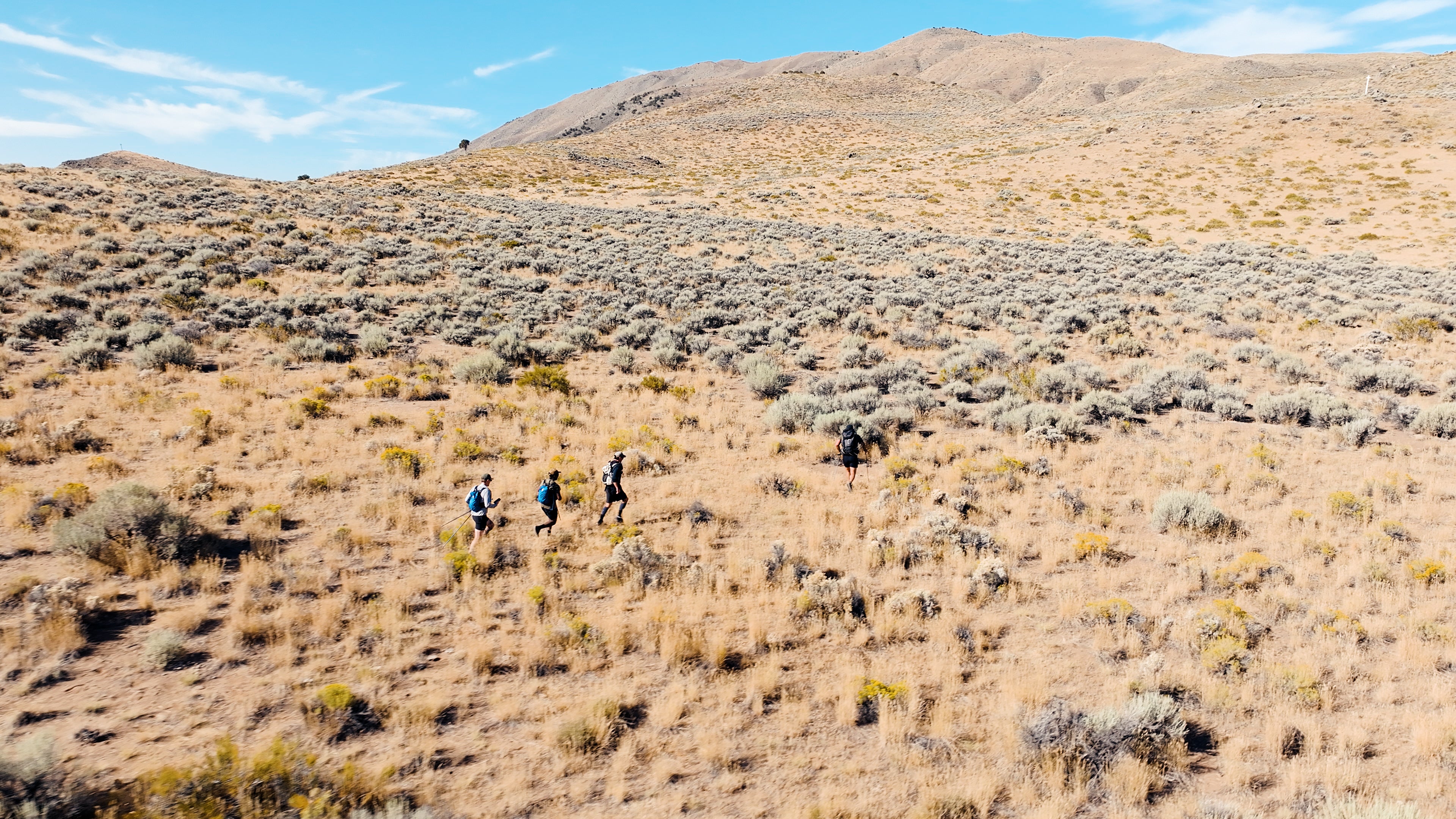 Three people hiking on a dry, hilly landscape with a clear blue sky for the 20 Mountain 220.