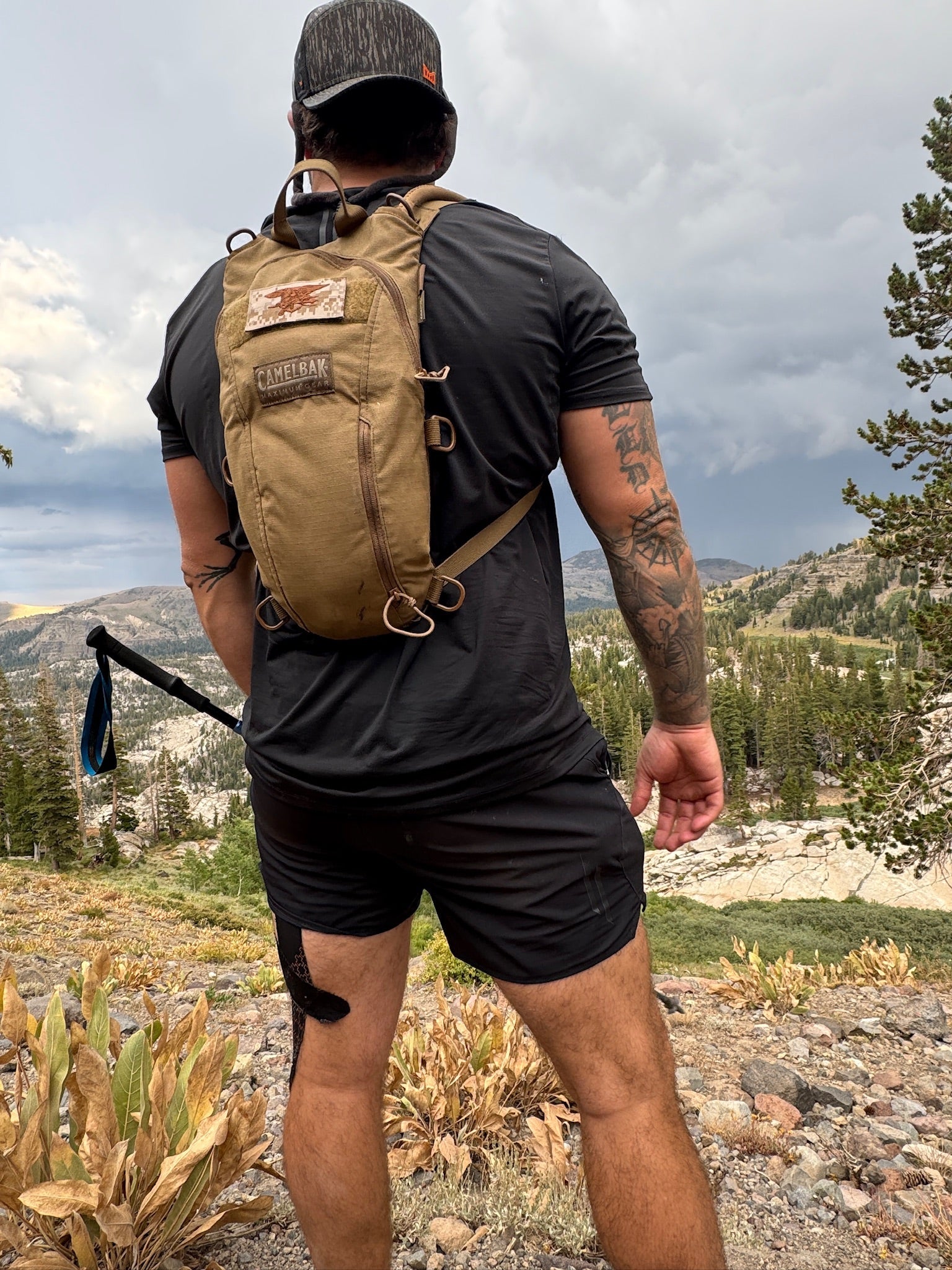 Navy SEAL Kyle Reed hiking with a backpack in a mountainous area wearing LINEAR Baseline series shirt and shorts in night ops black color.