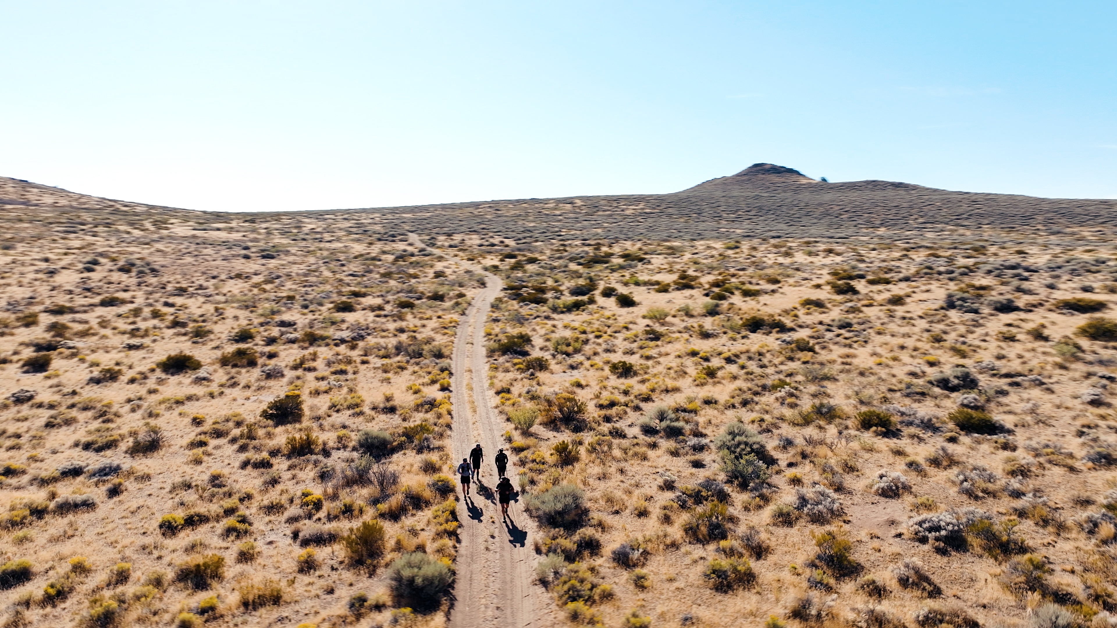 Desert landscape with a dirt path and two people walking away from the camera during the 20 Mountain 220 journey.