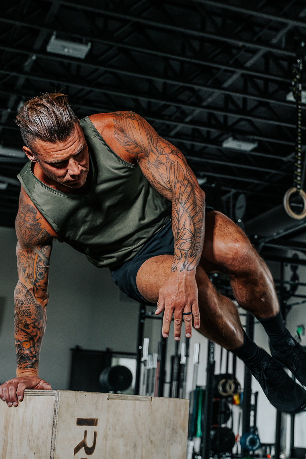 Man performing a box jump in a gym setting with ODA Green Baseline Tank on