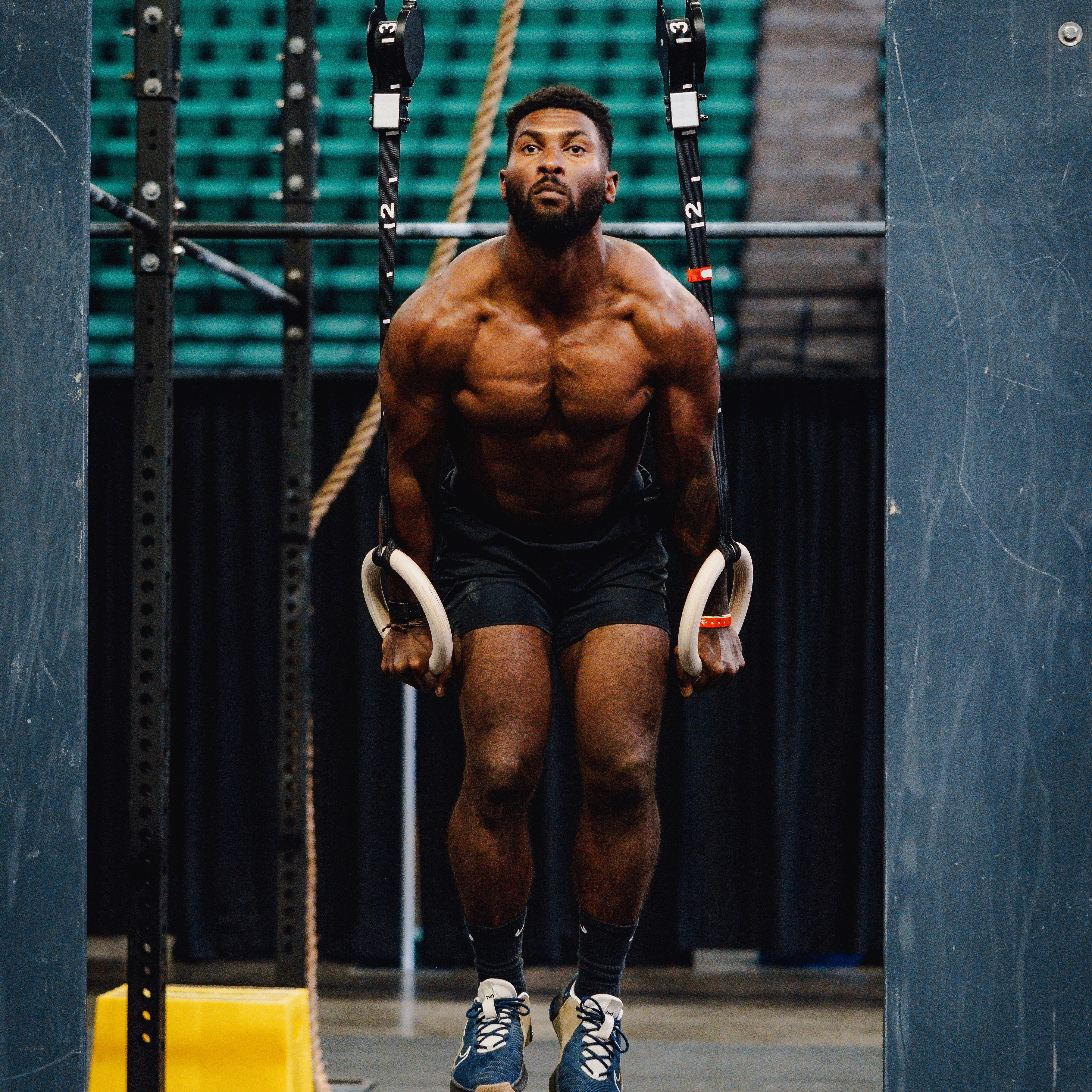LINEAR athlete Kody Dickerson doing muscle ups on rings in a gym setting at the Magic City Games wearing the LINEAR Baseline Series shorts in Night Ops Black.