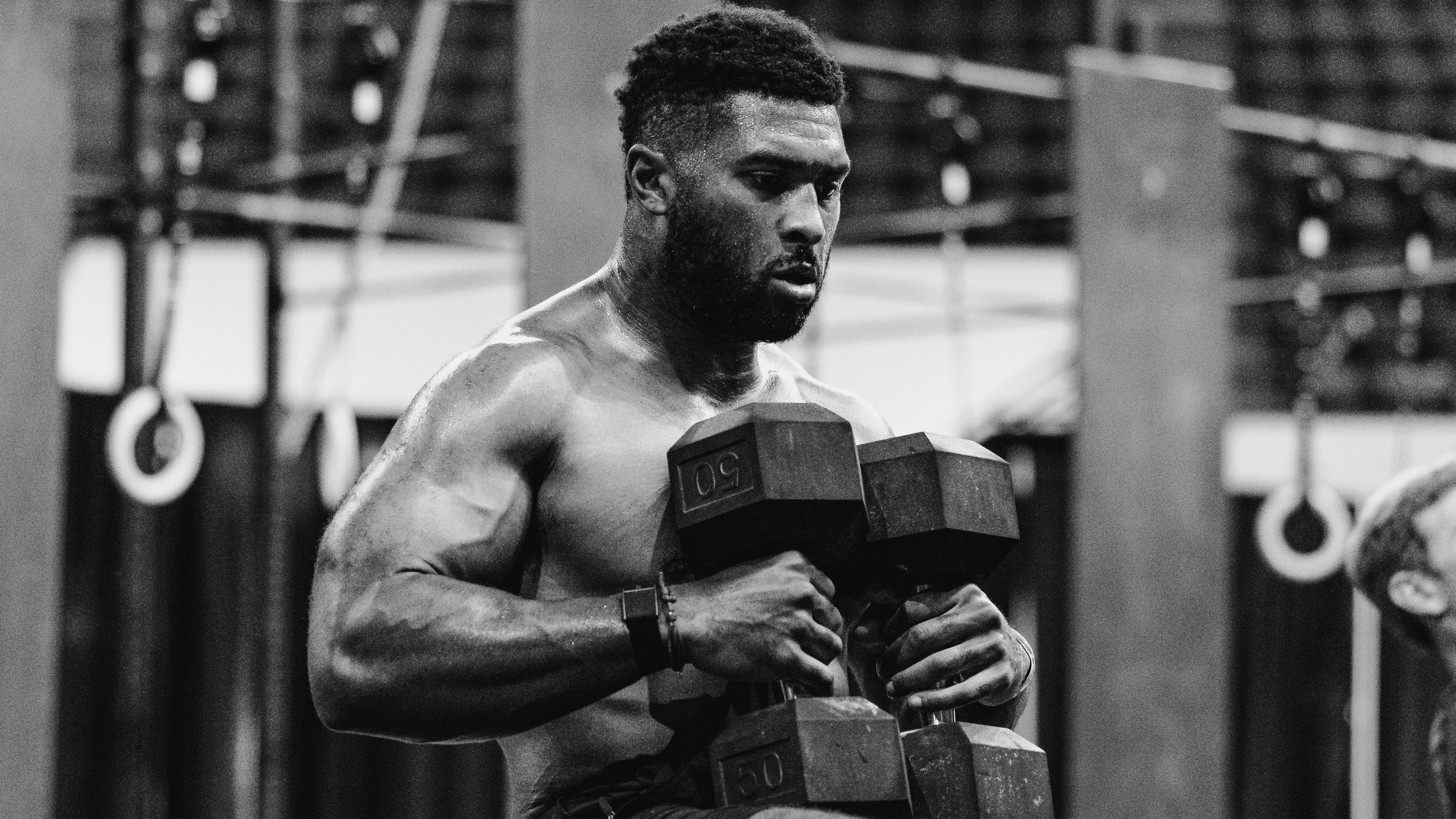 LINEAR athlete Kody Dickerson sitting on a bench with dumbbells on his lap in a gym setting at the Magic City Games wearing the LINEAR Baseline Series shorts in Night Ops Black.