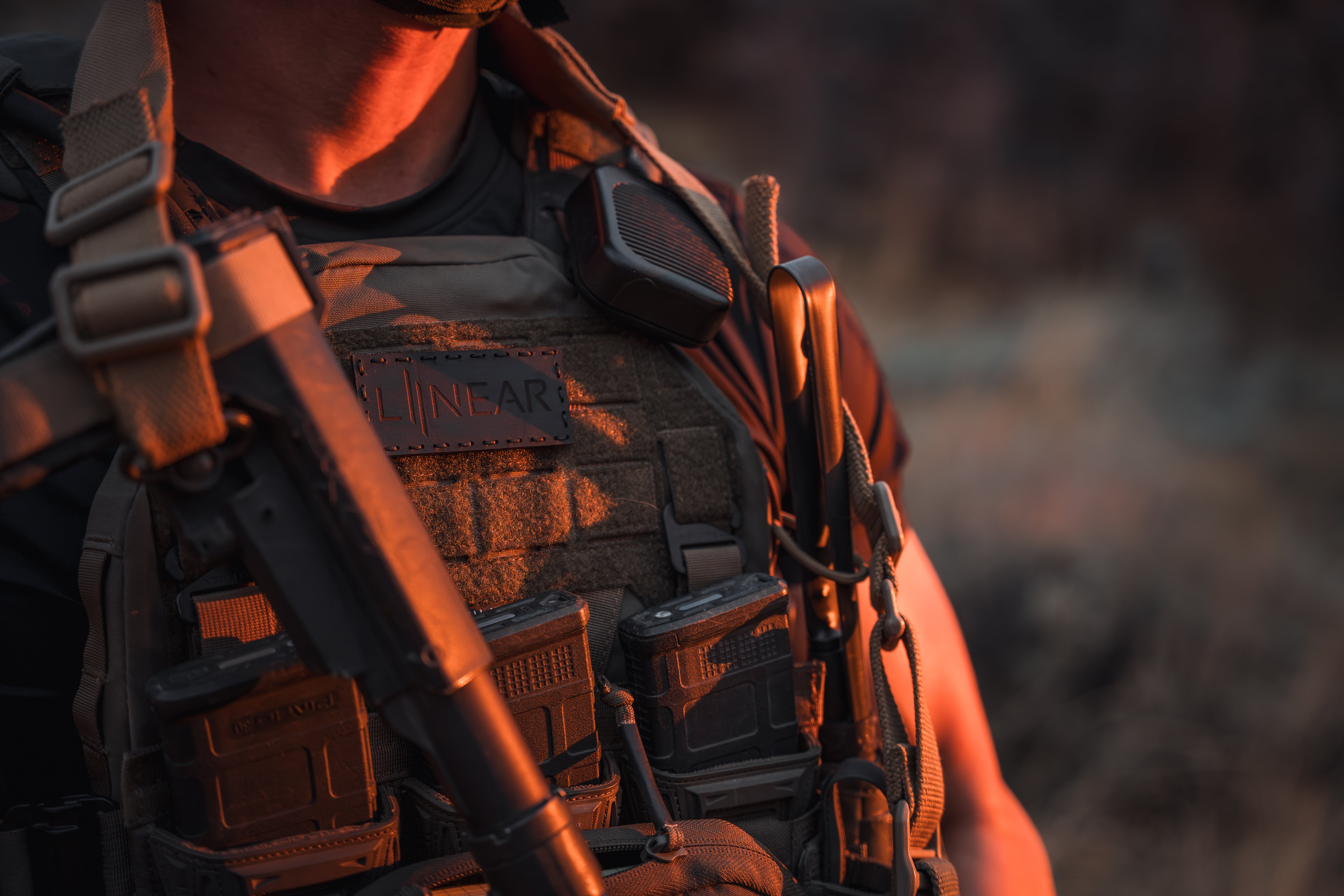 Person wearing a tactical vest with he LINEAR x Moral Decay Patchwork elite patch in a warm-toned setting.