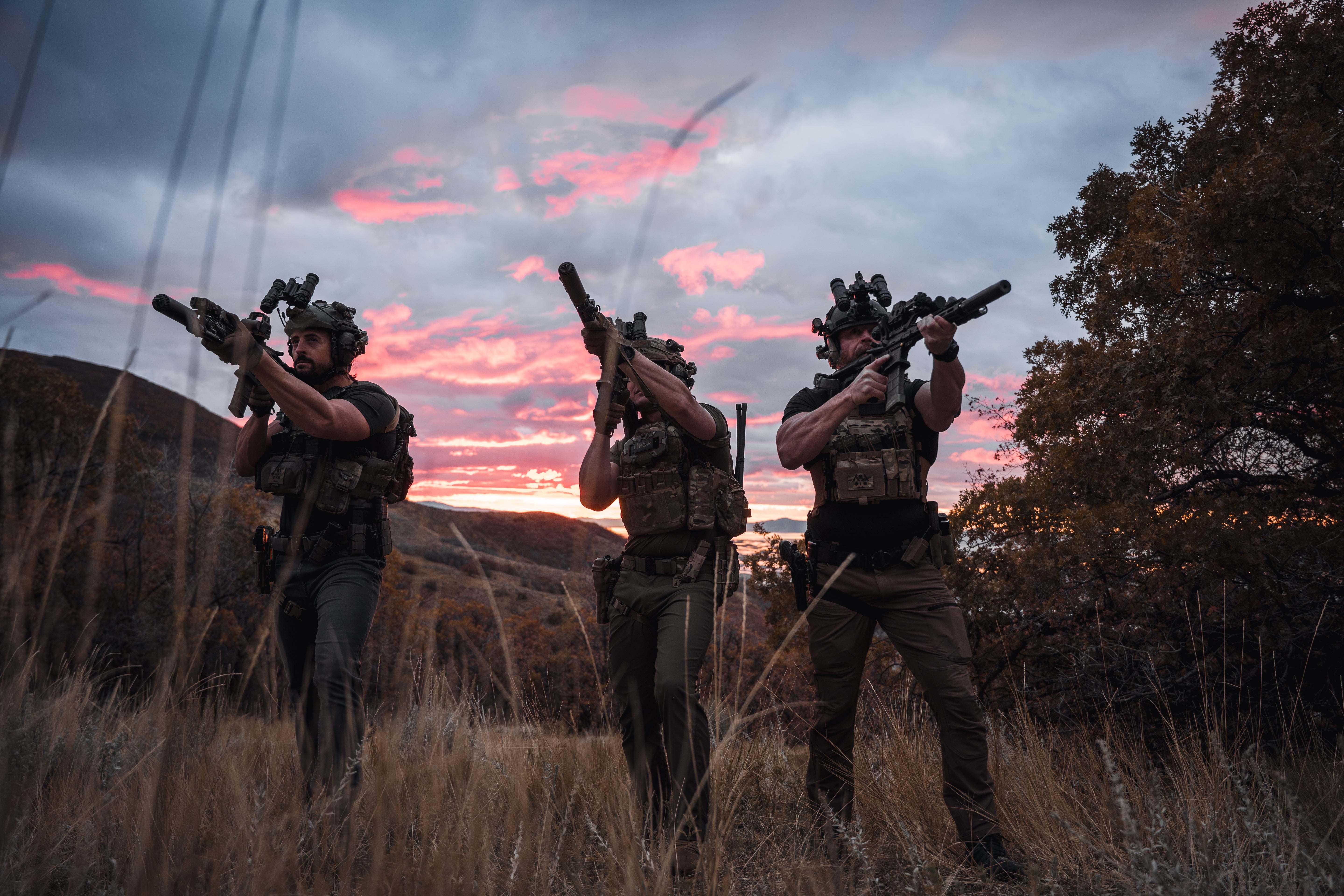 Three soldiers in tactical gear holding rifles against a sunset sky wearing the LINEAR x Moral Decay Patchwork elite and team patches on their kits.