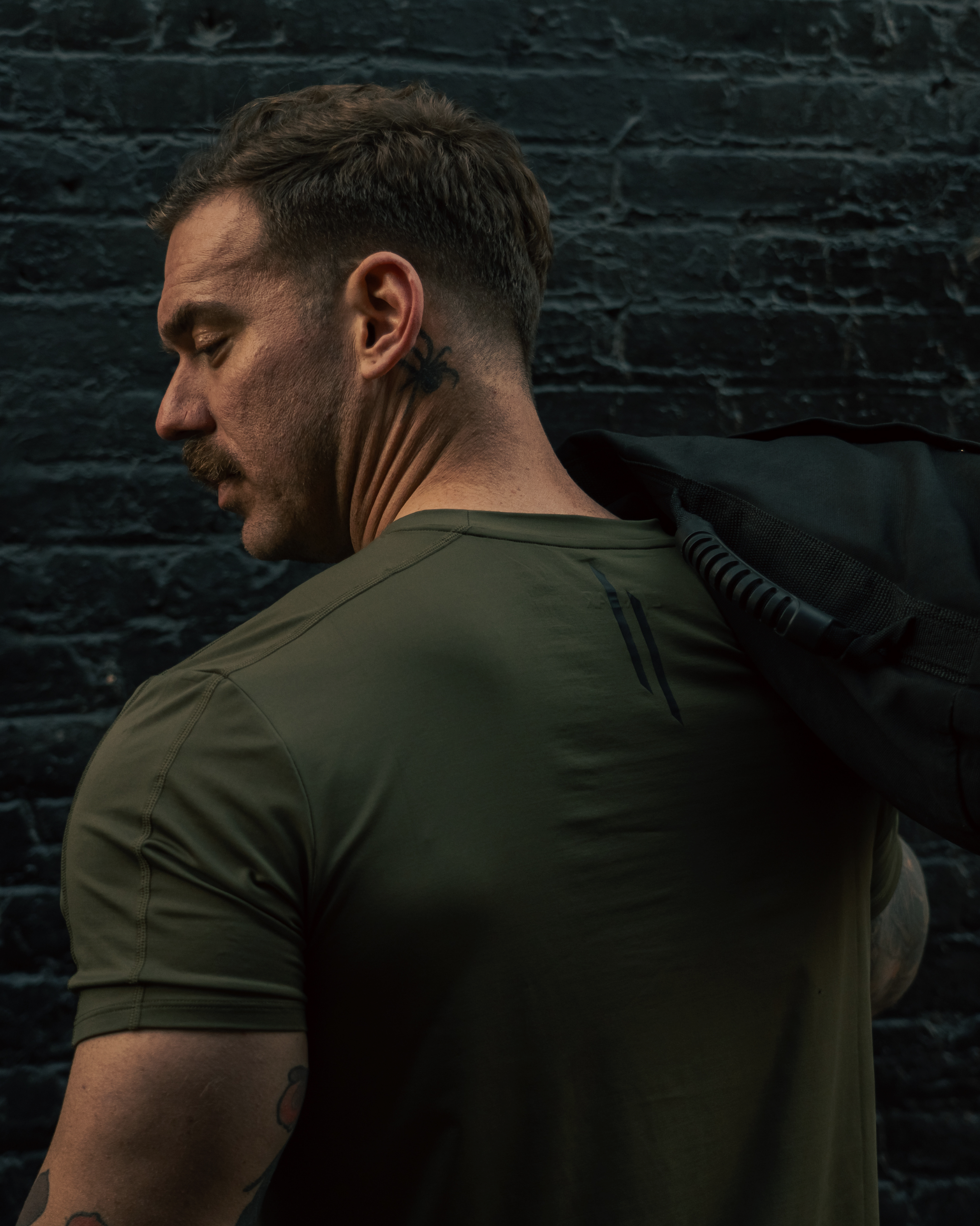 Man wearing a green t-shirt against a dark brick wall