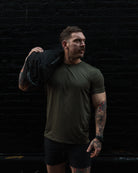 Man in green t-shirt and black shorts holding a sandbag against a dark textured wall