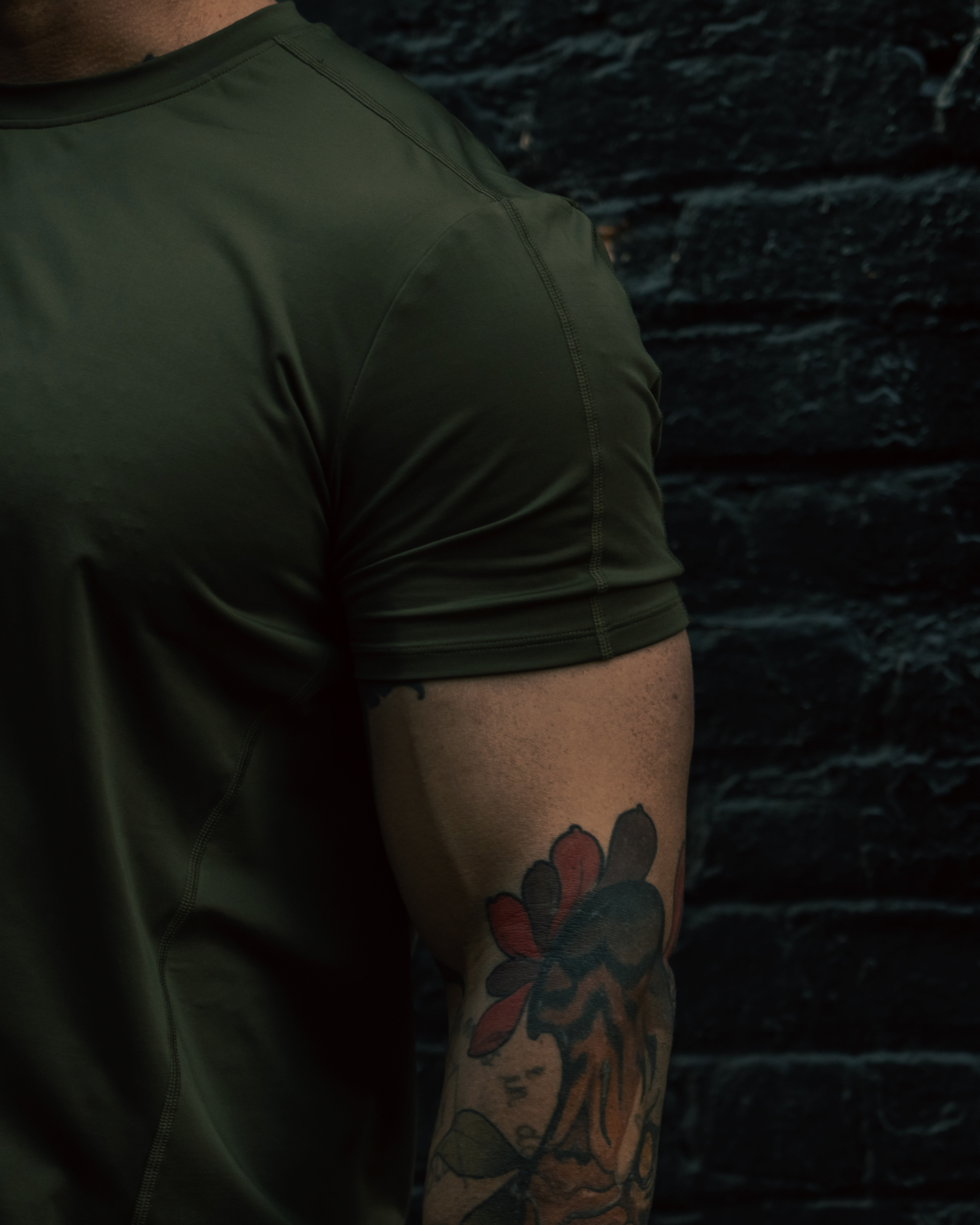 Person wearing a green t-shirt with a dark textured wall background