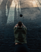 male launching weighted sand ball upwards against dark brick wall.