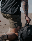 Person in a desert setting with a backpack, wearing a black shirt and green shorts.