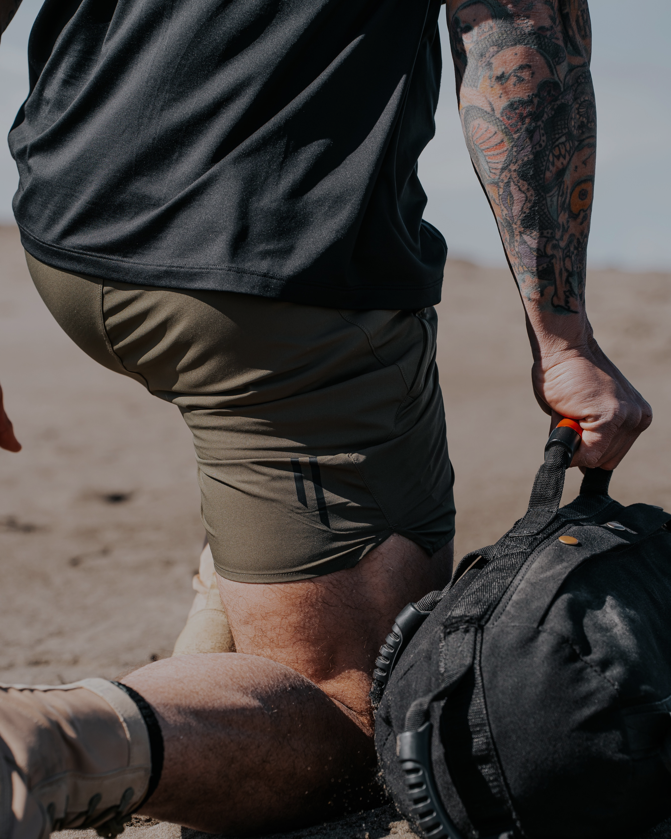 Person in a desert setting with a backpack, wearing a black shirt and green shorts.