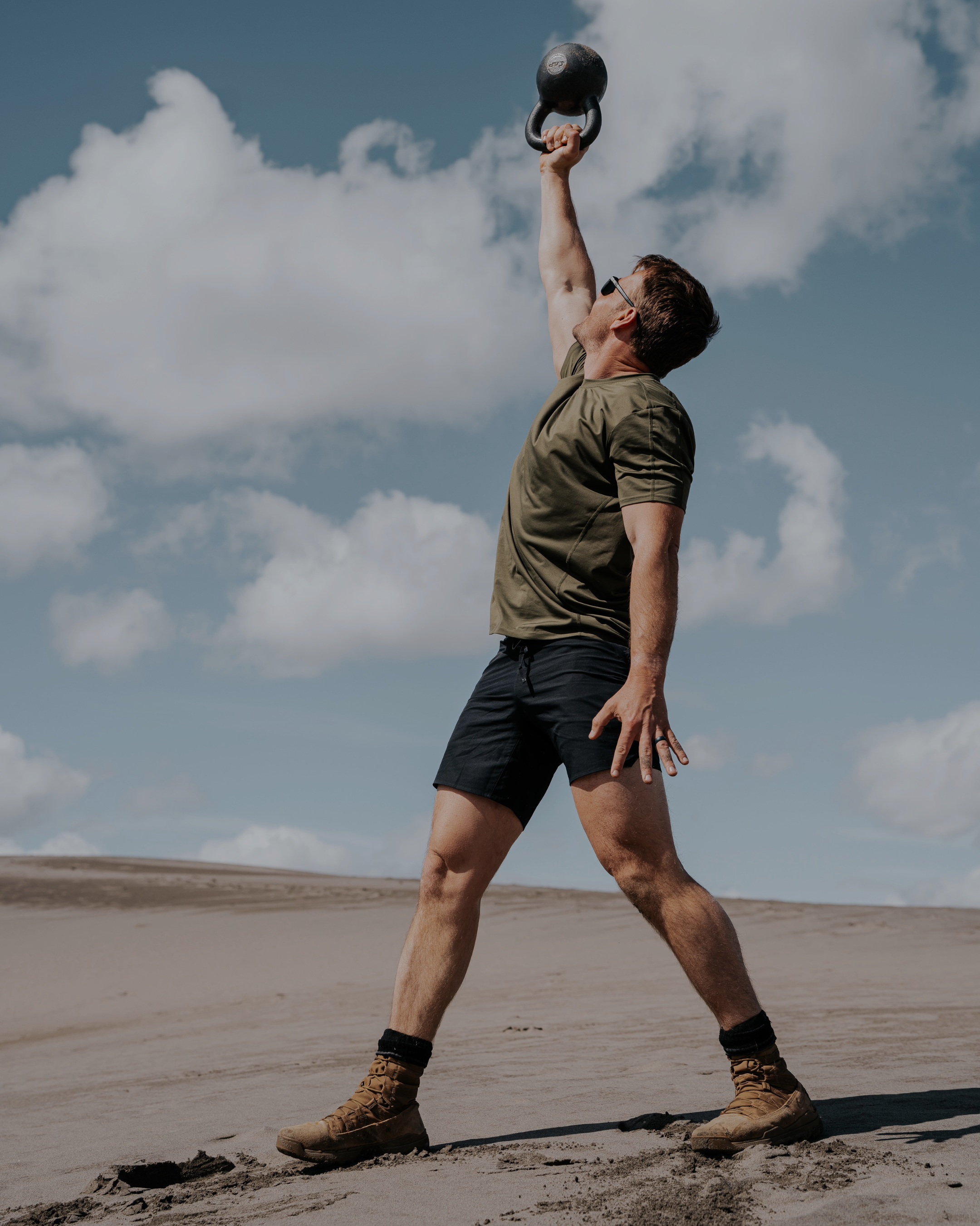 Man lifting a kettlebell outdoors with a clear sky in the background