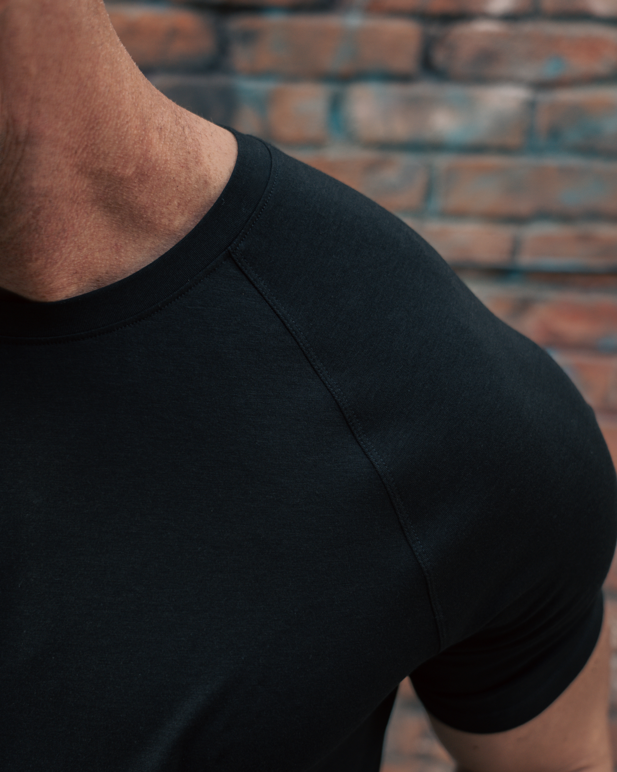 Person wearing a black t-shirt against a brick wall.