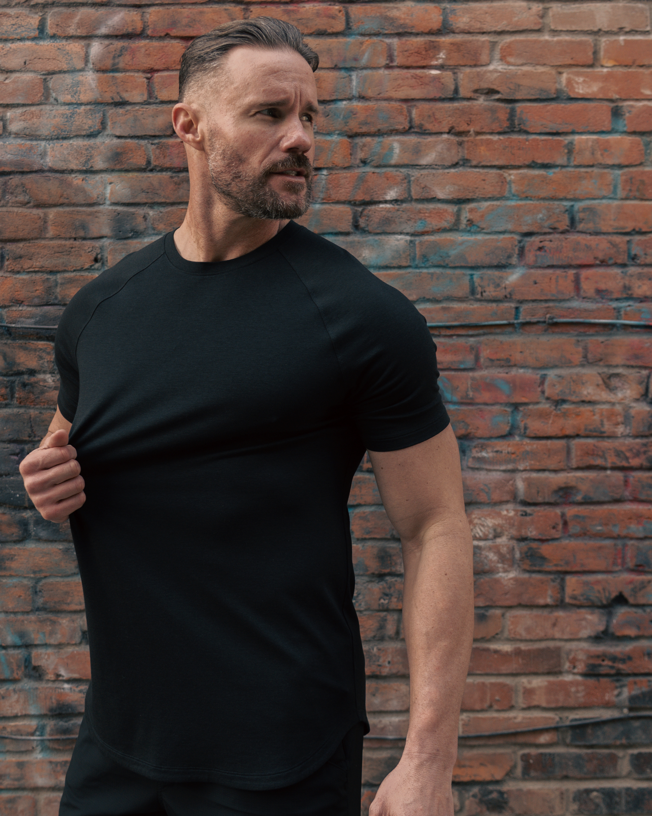 Man wearing a black t-shirt against a brick wall