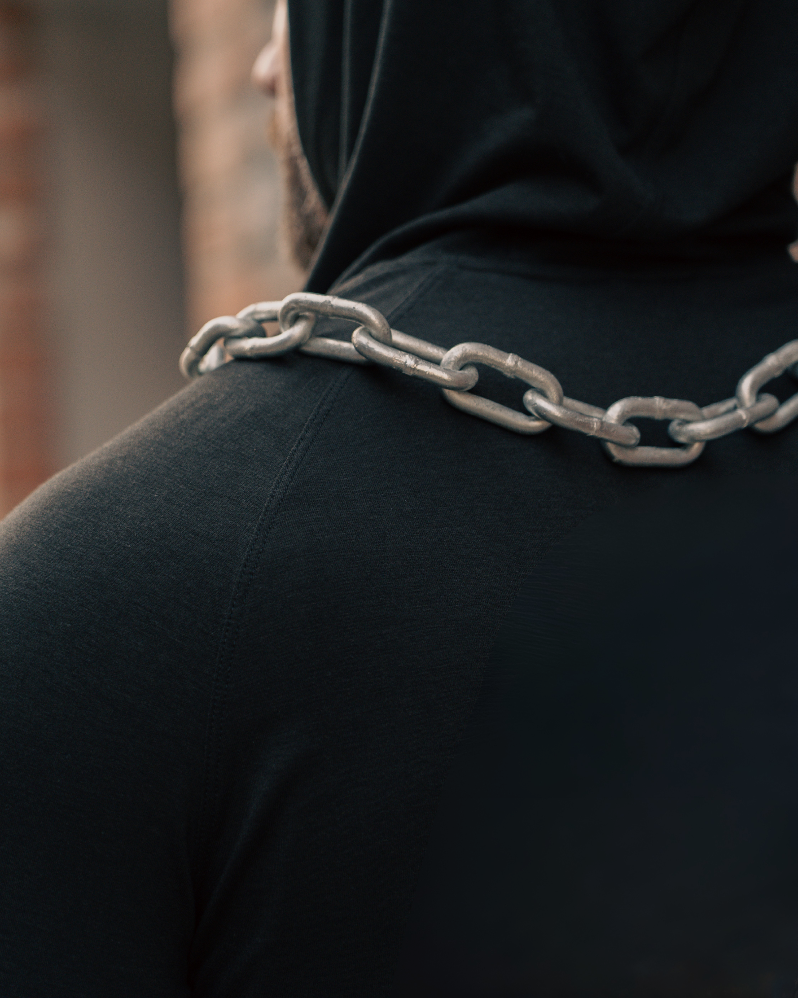 Person wearing a black hoodie with a chain around their neck, blurred background