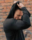 Man wearing a black hoodie against a brick wall