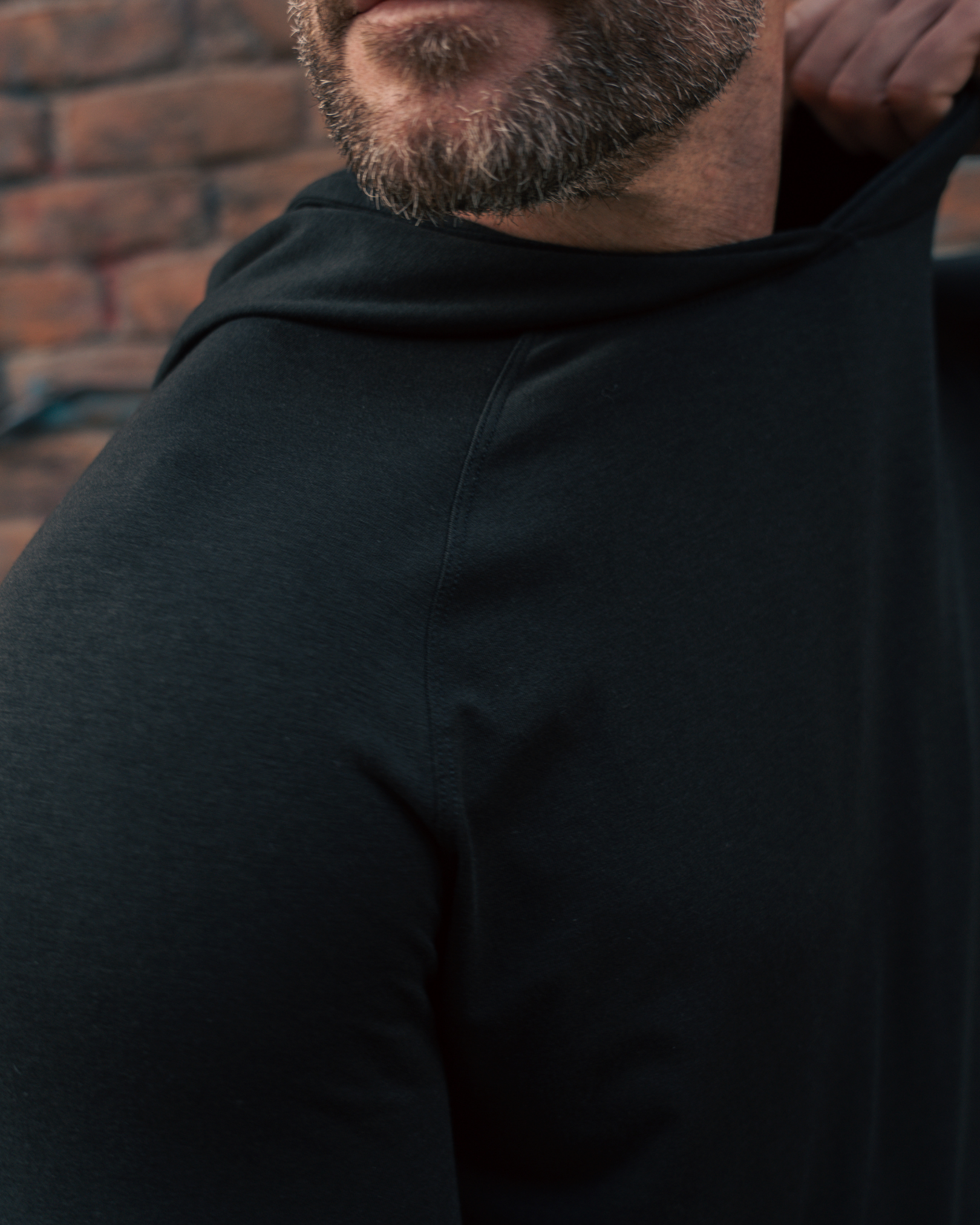 Man wearing a black hoodie with a brick wall background