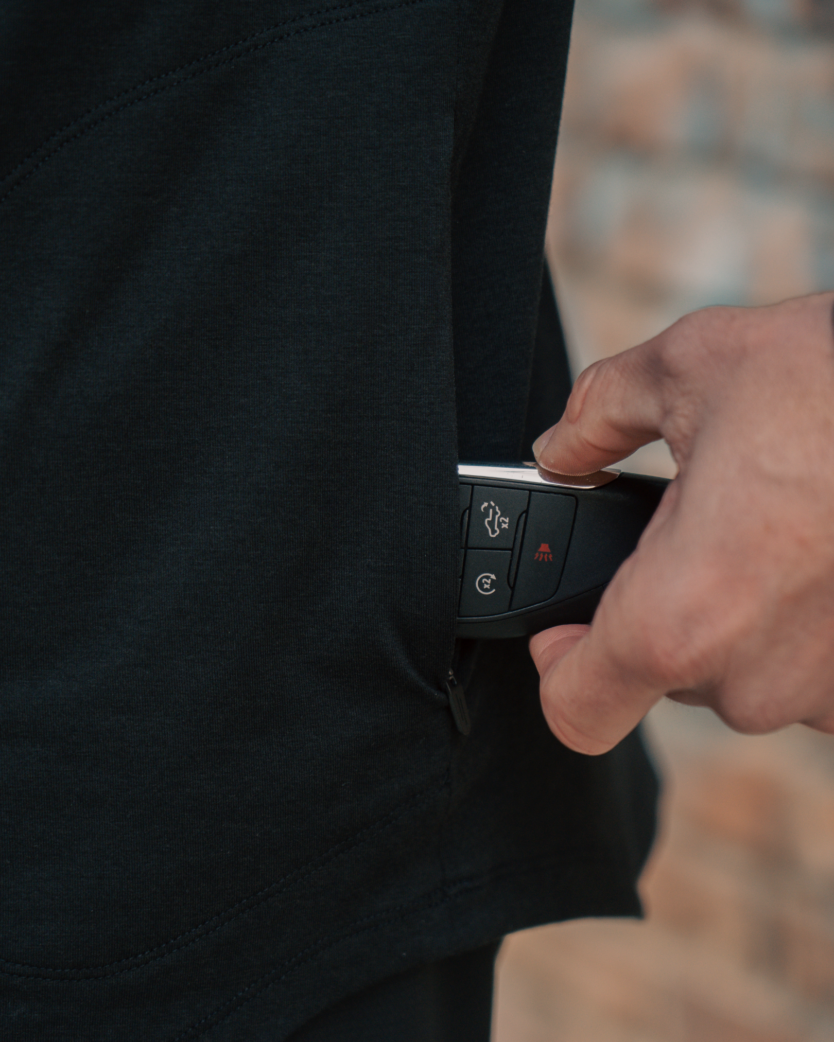 black hoodie on male placing key in side zip pocket.