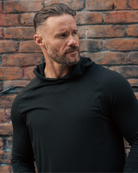 Man wearing a black hoodie against a brick wall