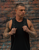 Man with tattoos holding chains against a brick wall