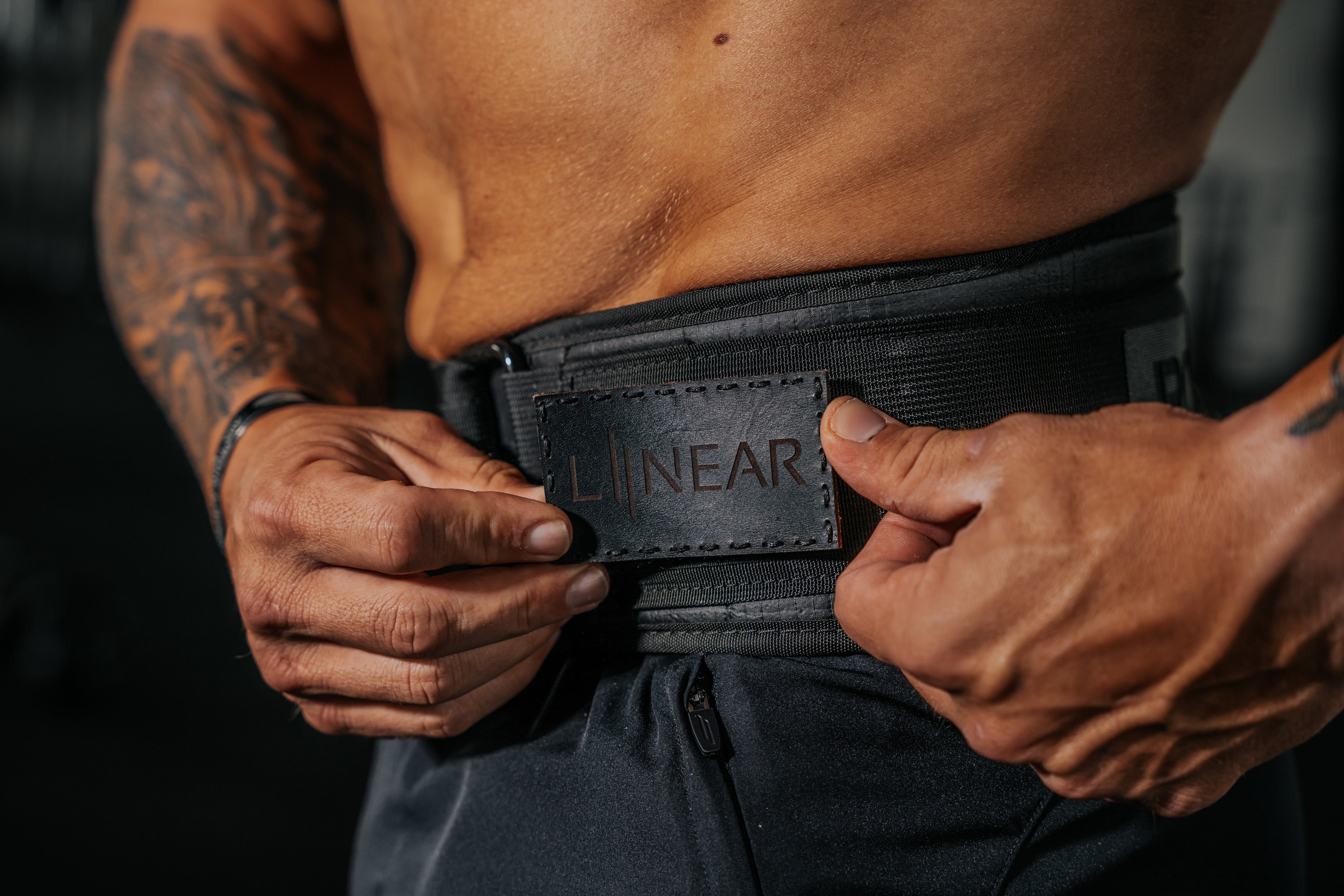 Person wearing a black weight belt with Night Ops Black LINEAR® Team Patch, focusing on the waist area.
