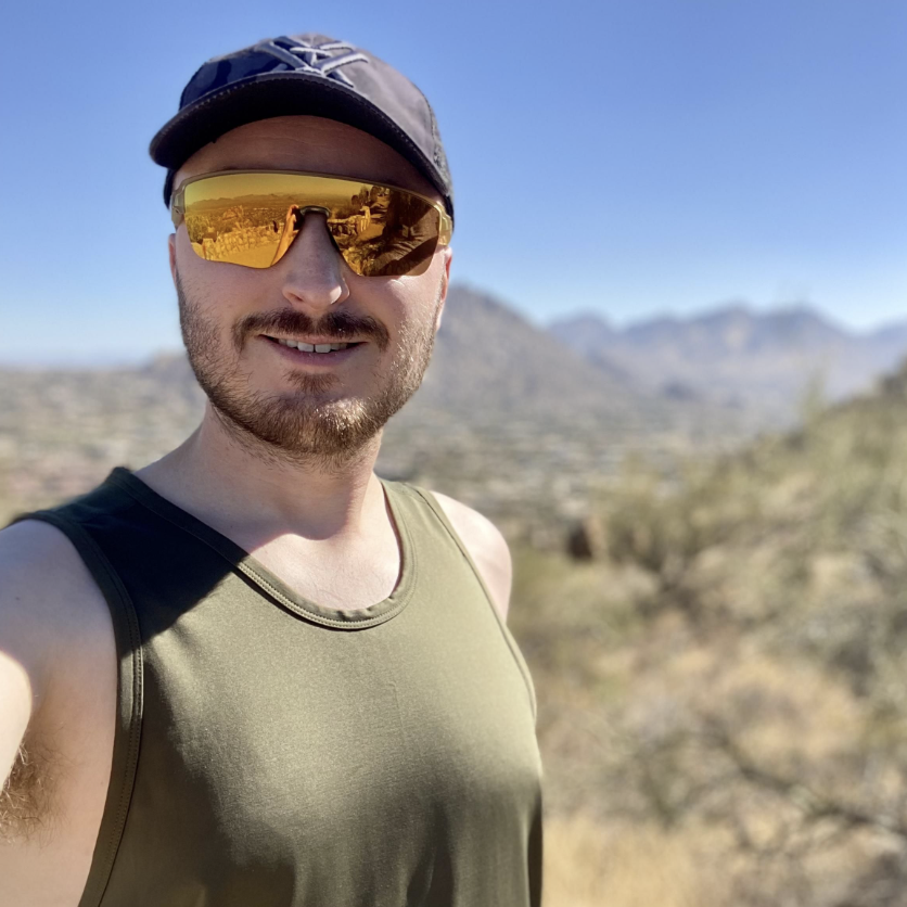 LINEAR® customer Jeffrey V wearing sunglasses, a cap and Baseline series tank in ODA green in a desert landscape with mountains in the background