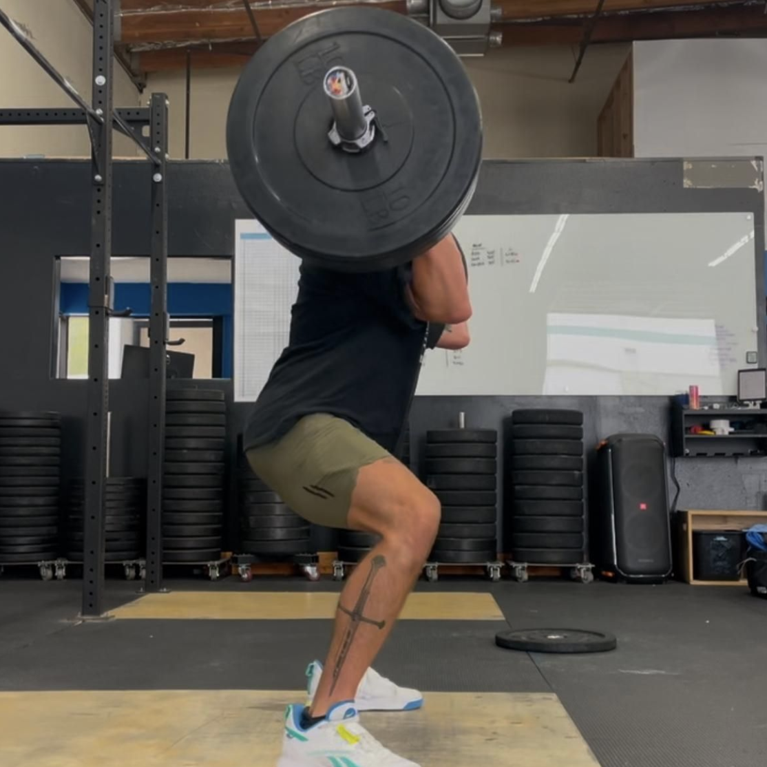LINEAR® customer Joeseph G performing a barbell squat in a gym setting wearing the baseline series shorts in ODA green