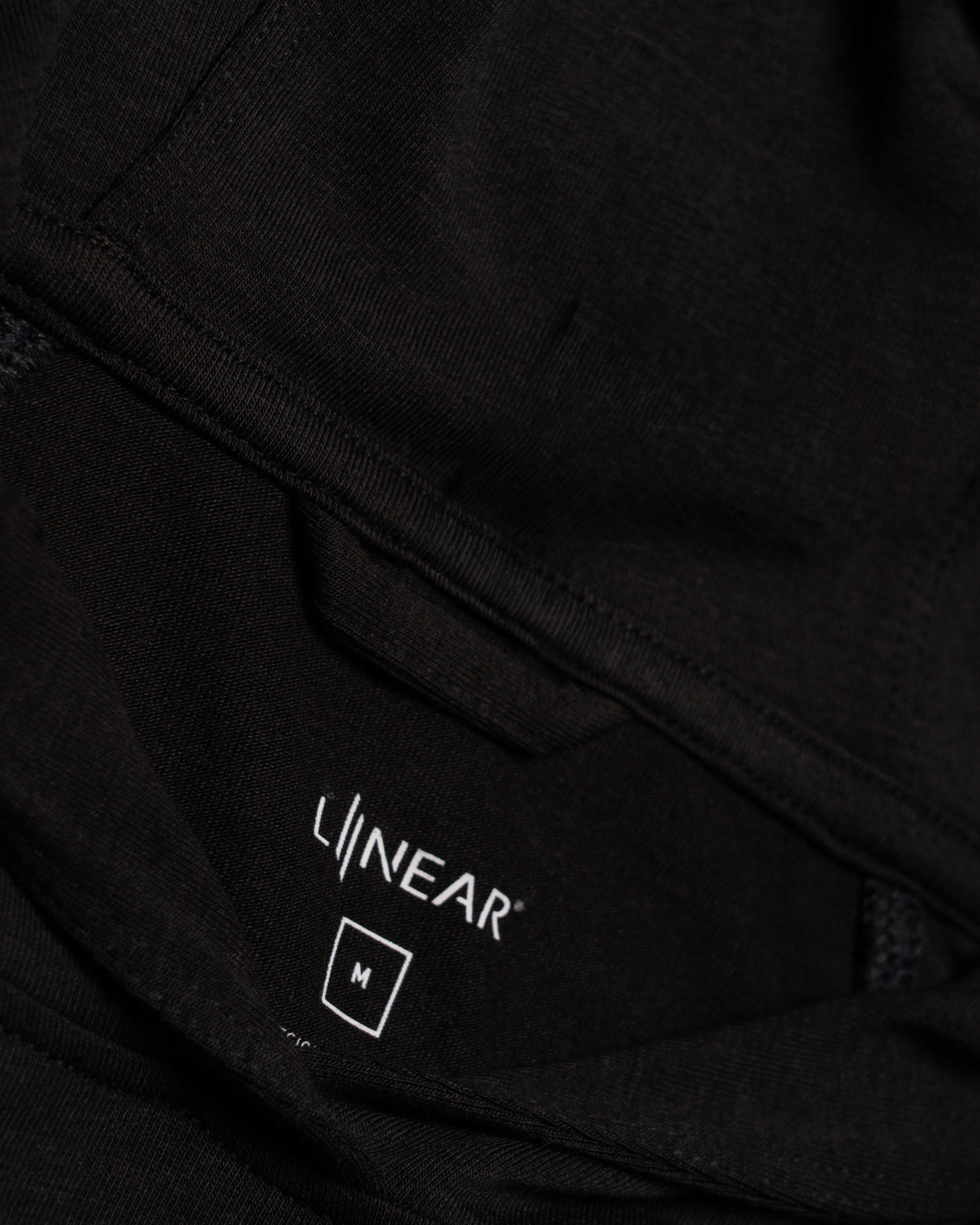Close-up of a black hoodie with 'LINEAR' logo on the chest pocket.